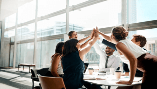 Team-tycoonstory | tycoonstory media Diverse business team giving a high-five during a meeting, symbolizing teamwork, success, and shared business goals in a modern office.