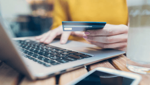 Transaction charges-tcoonstory | tycoonstory media Person making an online payment with a credit card on a laptop, representing visa interchange charges in digital transactions.