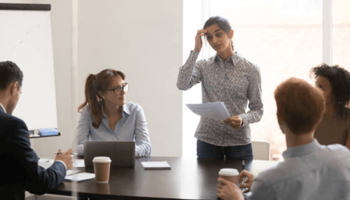 Overcome procrastination-tycoonstory | tycoonstory media Team in a meeting while a woman presents with notes, demonstrating time management skills during a well-organized workplace discussion.