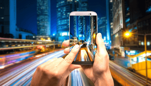 The transformation of the casino industry - tycoonstory | tycoonstory media From desktop to mobile: a person capturing the vibrant cityscape using a smartphone, showcasing mobile technology.