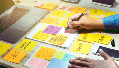 Startup strategy-tycoonstory | tycoonstory media Entrepreneurs planning digital marketing strategies using colorful sticky notes and a laptop on a workspace.