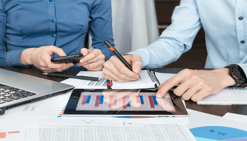 Taxing individuals in other states Two professionals reviewing charts and financial reports on a tablet and notepad while discussing data related to california state taxes.