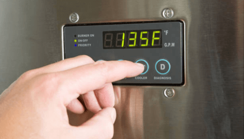 Water heather's temperature - tycoonstory | tycoonstory media A hand adjusting the temperature settings on a water heater's control panel, indicating the precise heat regulation.