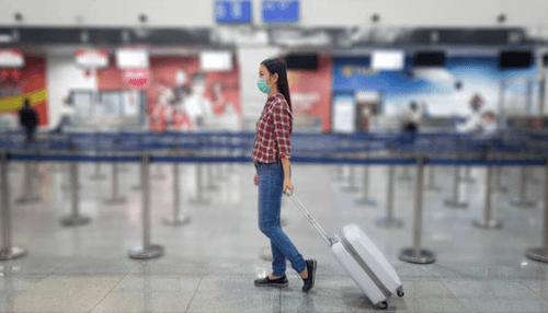 Travel warnings A woman wearing a mask and carrying a suitcase in an airport, ready for her christmas holiday travel.