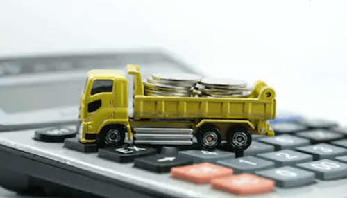 Benefits of truck factoring A toy dump truck loaded with coins on top of a calculator, illustrating the financial aspects and benefits of truck factoring in the transportation sector.