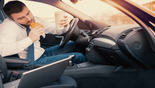 Distracted driving accident A businessman multitasking—eating, drinking, and talking on the phone in his car—leading to distracted driving accident risk.