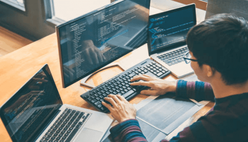 Technology related business ideas A person coding on multiple screens, reflecting the role of technology and programming in running and growing technology-related businesses.