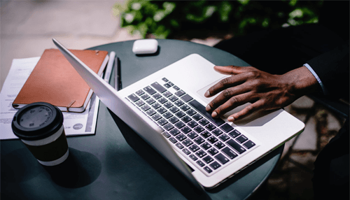 Flight booking-tycoonstory (1) | tycoonstory media Professional working on a laptop outdoors with documents and coffee, organizing tasks for their next business trip.