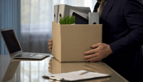 Best excuses to quit a job A person in a suit carrying a box filled with office supplies and documents, symbolizing leaving a job and transitioning out of the workplace.