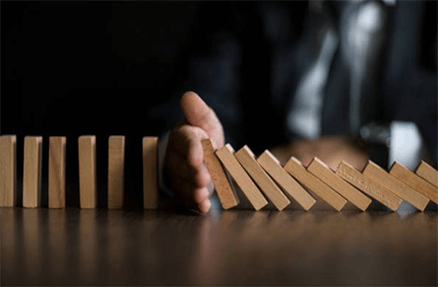 Challenges faced and how to avoid ecommerce failures-tycoonstory | tycoonstory media A person’s hand stopping falling dominoes on a table, symbolizing prevention or control of a potential problem.
