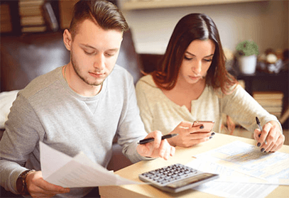 Filing taxes abroad as a us citizen-tycoonstory | tycoonstory media A young couple at a table working on filing taxes and using a calculator, paying attention to budgeting.