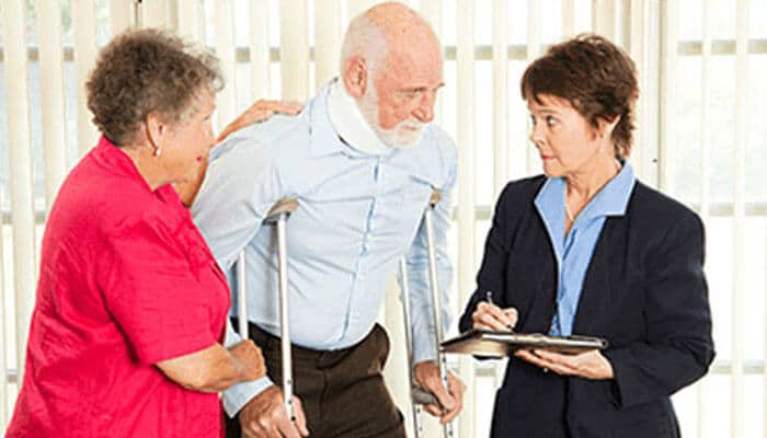 Lawyer assisting | tycoonstory media A lawyer assisting an elderly couple with paperwork related to a car accident injury, with the elderly man using crutches.