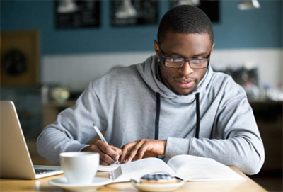 Business analyst A business analyst studying from textbooks and taking notes at a desk, preparing for certification exams with focused exam-clearing strategies.