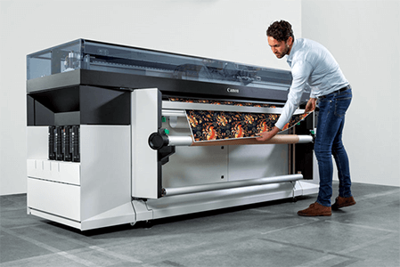 Industridesignsnyc professional printing services A person operating a large-format canon printer, feeding a roll of print material into the machine in a modern printing environment.