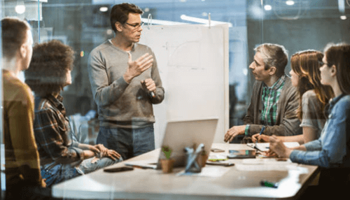 Starting a business A team gathered around a whiteboard discussing strategies and planning while starting a business.