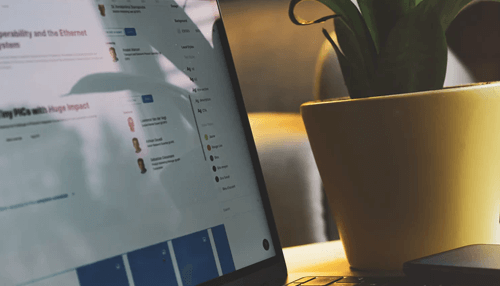 Choose an online platform to hire staff - tycoonstory | tycoonstory media Close-up of a laptop screen displaying business data and documents next to a plant in a workspace.