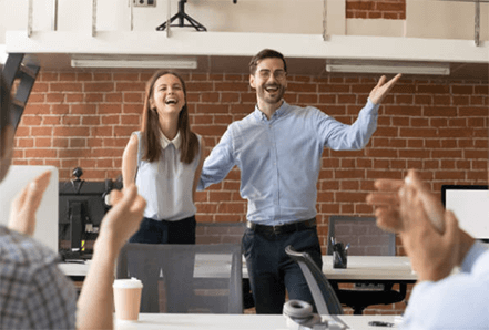 Employee appreciation day-tycoonstory | tycoonstory media Two employees smiling and posing during a celebration, with colleagues applauding them, emphasizing employee appreciation and recognition in a corporate setting.