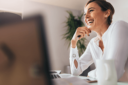 Happy employee-tycoonstory | tycoonstory media A woman smiling while sitting at her desk, likely engaging in work-related tasks, representing the positive impact of employee retention.