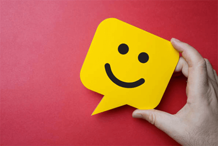 Keep current customers happy-tycoonstory | tycoonstory media A hand holding a yellow smiley face icon inside a speech bubble, symbolizing positive feedback and the successful launch of a business.