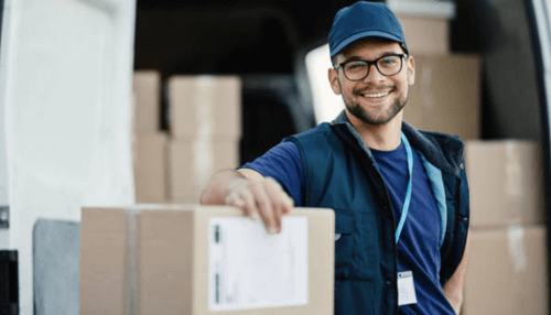 Move stress-free with nyc movers - tycoonstory | tycoonstory media Two movers in blue uniforms carrying large cardboard boxes, stepping away from the back of a moving truck with the rear door open.