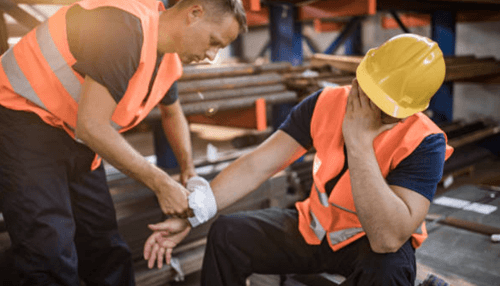 Some jobs are physically demanding - tycoonstory | tycoonstory media Co-workers wearing safety vests assist an injured employee by bandaging his arm in an industrial setting, illustrating common workplace accidents and first-aid care.