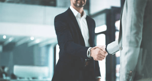 Tips on how to buy a business without investment-tycoonstory | tycoonstory media Two business professionals shaking hands in a modern office setting, symbolizing a successful business deal or partnership.