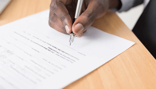 Gaming authorities - tycoonstory | tycoonstory media Close-up of a person signing an official document with a pen on a wooden desk.