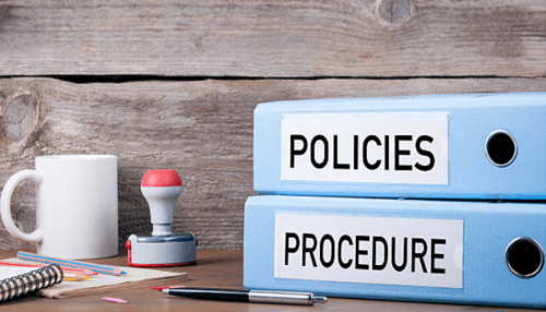 Irs guidelines for taxation Office desk with two labeled binders titled ‘policies’ and ‘procedure,’ symbolizing organizational rules and documentation.