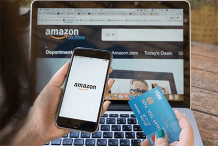 Amazon pay-tycoonstory | tycoonstory media Customer shopping on amazon using a smartphone and laptop while holding payment cards, illustrating how bigcommerce orders accommodate amazon pay for seamless online transactions.