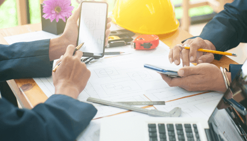 Be ready to prove how you can pay it back - tycoonstory | tycoonstory media Commercial loan discussion between construction professionals reviewing architectural plans, smartphone data, and project documents at a work desk with safety helmet and tools.