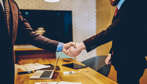 Businesses with sponsored events - tycoonstory | tycoonstory media Business professionals shaking hands over a desk after finalizing a sponsorship agreement during a corporate meeting.