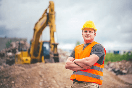 Protect head with hard hat A construction worker wearing ppe with a hard hat and safety vest standing confidently at a worksite.