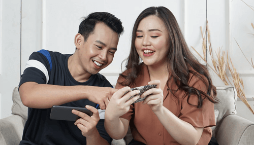 Playstation and the xbox - tycoonstory | tycoonstory media Smiling couple reviewing information on a smartphone together, discussing personal finances and planning a business loan for future goals.