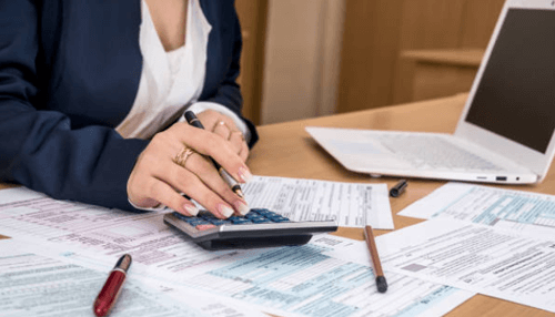 Save money by paying less in corporate taxes - tycoonstory | tycoonstory media Business professional calculating financial documents using a calculator and laptop, representing accounting and tax preparation tasks.