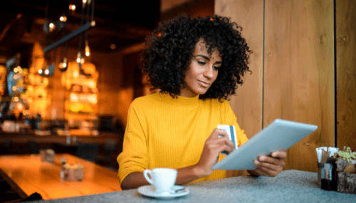 Smarter stock purchasing decisions - tycoonstory | tycoonstory media A woman using a tablet and credit card while enjoying coffee, representing digital payments in a small business café.