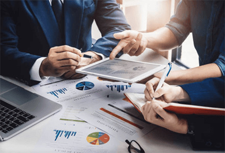 Benefits of financial management to the success of a business-tycoonstory | tycoonstory media A group of business professionals gathered around a table with a tablet and numerous charts and graphs, discussing strategy and reviewing reports related to financial management.