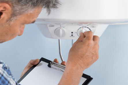 Water pipes-tycoonstory | tycoonstory media Technician adjusting the water heater's settings, while holding a clipboard for inspection, symbolizing maintenance and plumbing work related to slab.