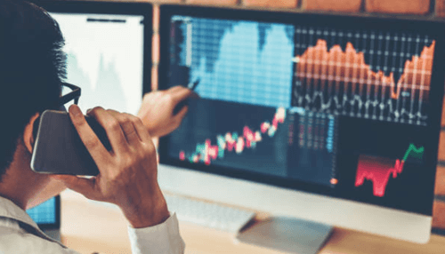 Find new investment ideas using a stock screener - tycoonstory | tycoonstory media Trader analyzing stock screener charts on computer while making a phone call for market insights.
