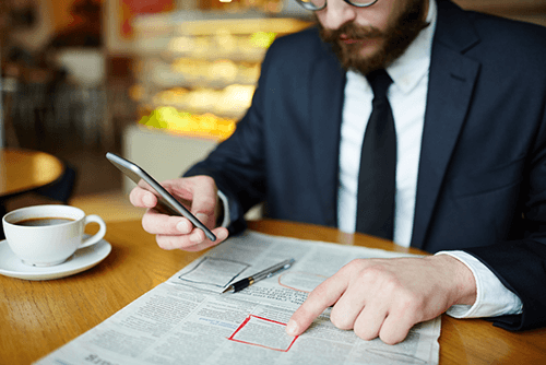 Job advert tips-tycoonstory | tycoonstory media A man, dressed in a suit, pointing at a job advert, as depicted on a back-page newspaper advertisement, depicts a job search process.