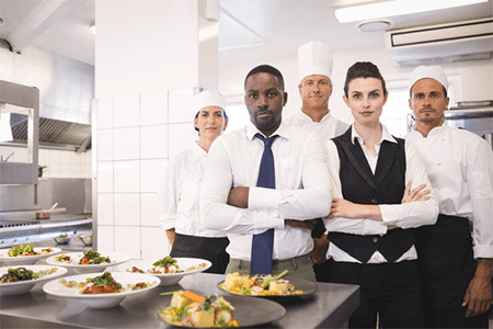 Quest food management services-tycoonstory | tycoonstory media A team of chefs and kitchen staff posing together in a professional kitchen, exemplifying effective food management in a restaurant environment.