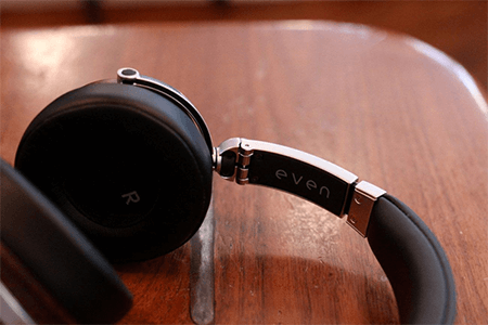Best personalized corporate gift idea-headphones | tycoonstory media Personalized corporate gifts for techies: black over-ear headphones with a silver hinge and brand name'even' engraved on the side, set on a wooden surface.
