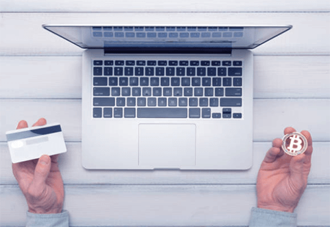 Bitcoin transactions-tycoonstory | tycoonstory media A laptop with a person holding a credit card in one hand and a bitcoin coin in the other, symbolizing digital payments.