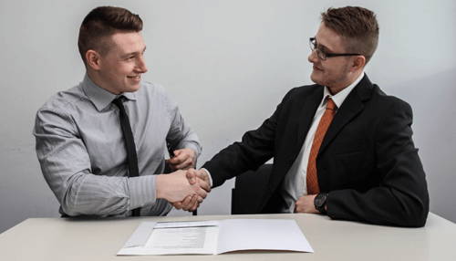 Customer retention - tycoonstory | tycoonstory media Two businessmen shaking hands over a document, representing customer retention and business trust.