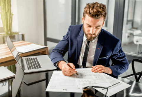 How entrepreneurs should manage risks in their start-ups-tycoonstory | tycoonstory media A man in a suit working on business documents at a desk, representing the strategic planning and organization required for start-ups.