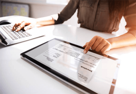 Invoice factoring-tycoonstory | tycoonstory media Business professional reviewing an invoice on a tablet, with a focus on invoice factoring, part of effective purchase order financing strategies