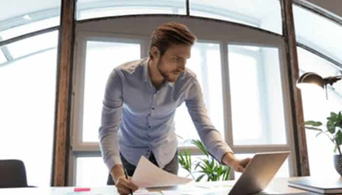 Professional reviewing documents | tycoonstory media Professional reviewing documents and planning tasks on a laptop, working to prevent project management mistakes through better organization