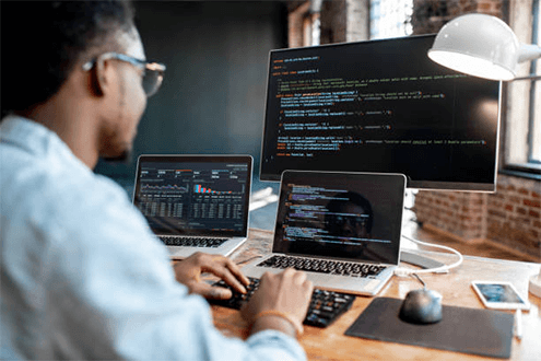 Tips to choose the best software development company-tycoonstory | tycoonstory media A man wearing glasses working on a multi-screen setup, actively engaged in software development.