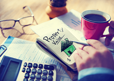 Proven ways to maximize your property value-tycoonstory | tycoonstory media Hand writing property value with a drawing of a house in a notebook, next to a calculator, documents, and a coffee cup on a desk.