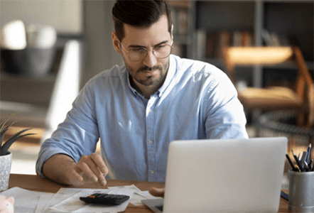 Tips for choosing client portal software-tcoonstory | tycoonstory media A man working on his laptop with papers and a calculator, indicating the use of client portal software for business management.