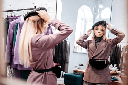 Hat selection based on facial feature-tycoonstory | tycoonstory media A smiling blonde woman wearing a dark red, sleeveless dress and a wide-brimmed straw hat is standing outdoors in a lush, green, sunlit garden or greenhouse. This is a bright, summery hat style for women.